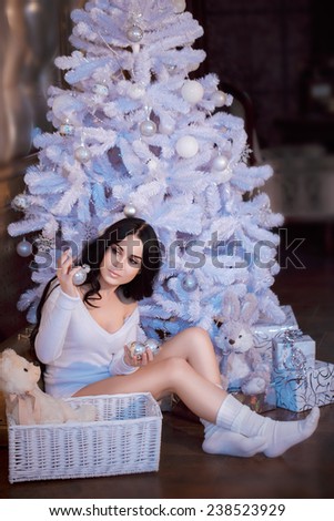 Young beautiful brunette woman in a white sweater and white socks decorates the Christmas tree toys. Christmas and new year concept.