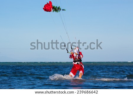 Young man on the kite in the costume of Santa Claus with a Christmas tree in the bag . Christmas and New year on a tropical island. Extreme Sport Kitesurfing