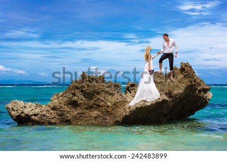 Happy bride and groom having fun on a tropical beach under the palm trees. Tropical sea in the background. Summer vacation concept.