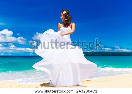 beautiful brunette bride in white wedding dress with big long white train and with wedding bouquet stand on shore sea