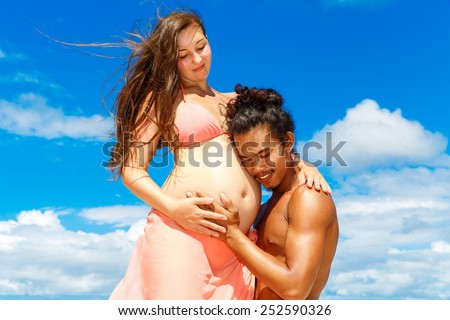Happy and young pregnant couple having fun on a tropical beach. Summer vacation. New life concept. Future mother and father.