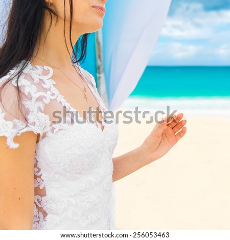 Bride giving an engagement ring to her groom under the arch decorated with flowers on the sandy beach. Wedding ceremony on a tropical beach in blue. Wedding and honeymoon concept.