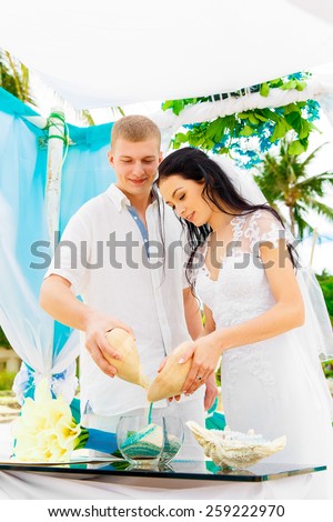 Wedding ceremony on a tropical beach in blue. Sand Ceremony. Happy groom and bride under the arch decorated with flowers on the sandy beach. Wedding and honeymoon concept.