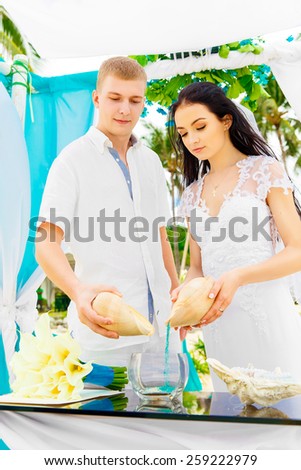 Wedding ceremony on a tropical beach in blue. Sand Ceremony. Happy groom and bride under the arch decorated with flowers on the sandy beach. Wedding and honeymoon concept.