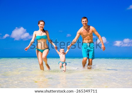 Happy family, mom, dad and little child having fun on a tropical beach. Summer vacation concept. Outdoor portrait of a happy family.