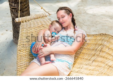 Happy family, mom and little child lie in a hammock on a tropical beach. Summer vacation concept. Outdoor portrait of a happy family.
