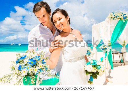 Wedding ceremony on a tropical beach in blue. Happy groom and bride under the arch decorated with flowers on the sandy beach. Wedding and honeymoon concept.