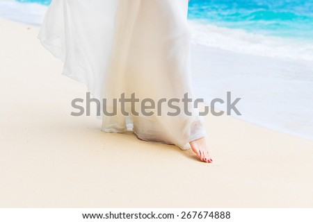 beautiful young bride in a white wedding dress walking on a tropical sandy beach. feet close-up.