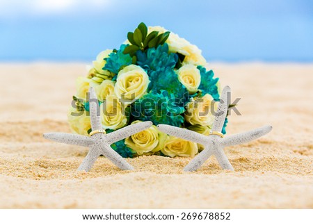 Two wedding rings with two starfish and wedding bouquet on a sandy tropical beach. Wedding and honeymoon in the tropics.