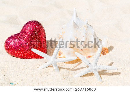 Two starfish, big red heart and large shell on a sandy tropical beach.
