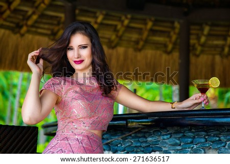 Beautiful girl sitting at the bar of the hotel on a tropical island and enjoying a cocktail.