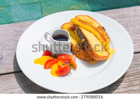 Delicious breakfast with french toasts with fried banana, honey and fresh fruit on a plate on old wooden background.
