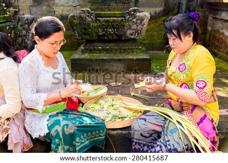Bali, Indonesia, May 3, 2015. Balinese women make decorations of palm leaves for the feast at the local temple in Bali, Indonesia. Offering flowers and other gifts is very popular tradition on Bali.