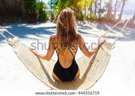 Young beautiful girl in black bathing suit with long blonde hair relaxing in hammock on the tropical beach