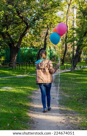 Teenager girl holding balloons and walking along the road in the park