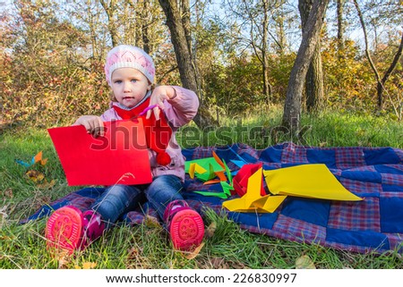 Little girl carves figures out of colored paper in the autumn forest