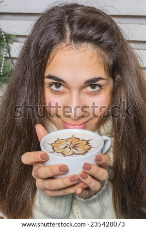 Beautiful and happy girl with gifts near a Christmas tree wishes everyone a Merry Christmas and Happy New year drinking cappuccino