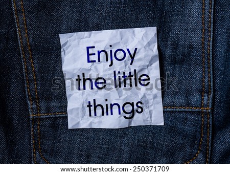 The inscription on the crumpled paper on jeans background. Enjoy the little things