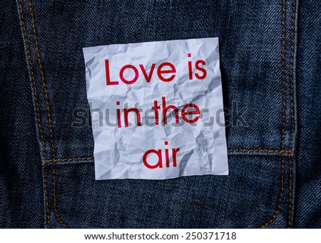 The inscription on the crumpled paper on jeans background. Love is in the air