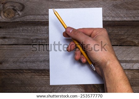 Colored pencils with white paper and pencil in male hand on vintage wooden background