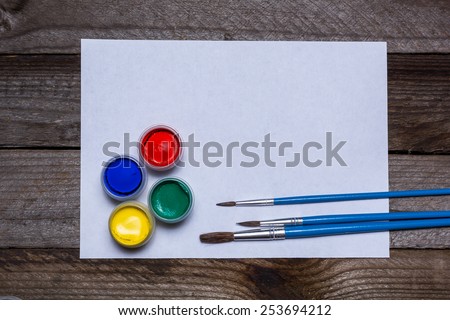 Brushes and yellow, red, green and blue paint for artist painter and paper on wooden background