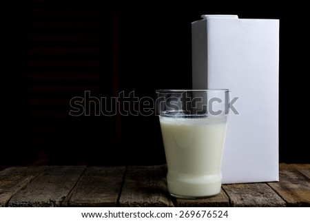 A carton of milk and a glass with a drink on a wooden vintage background