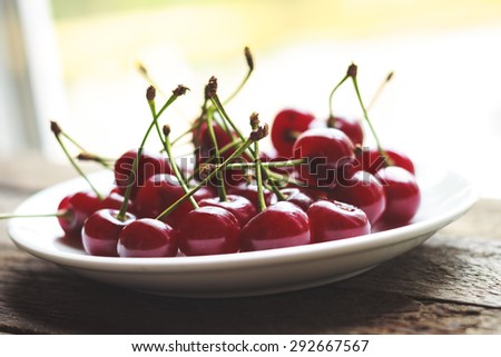 Ripe cherries on a plate on the wooden table, vintage