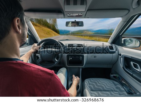 Man\'s hands of a driver on steering wheel of a car on road