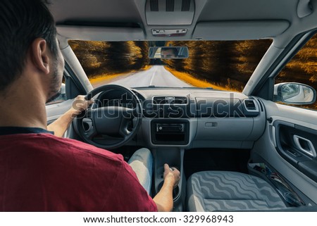 Man\'s hands of a driver on steering wheel of a car on autumn road