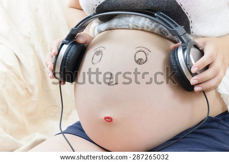 Pregnant woman tummy with smiley face and headphones