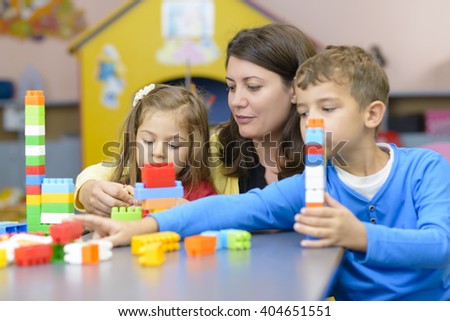 Kids and educator playing with plastic building blocks at kindergarten