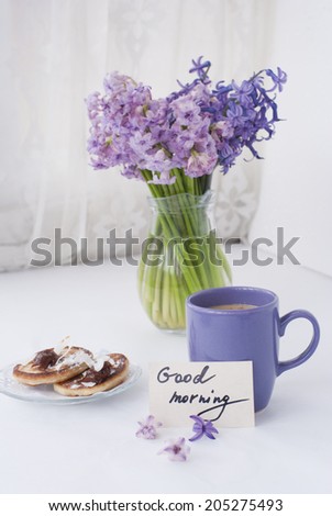Hyacinthus flowers in a transparent jar with god morning note, house candle holder and breakfast