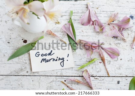Pink Astromeria flowers in a white jar vase with good morning note spread around