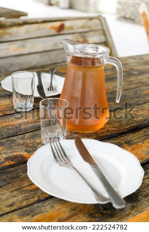 Georgian Wine Rqatsiteli served in a glass jar, two small wine glasses, cutlery, wooden surface, table