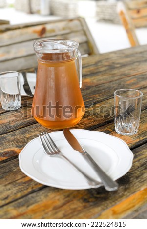 Georgian Wine Rqatsiteli served in a glass jar, two small wine glasses, cutlery, wooden surface, table