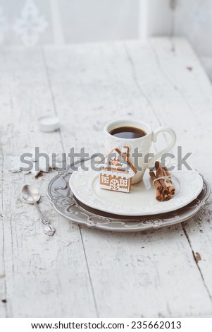 Shabby chic style coffee cup and plate with gingerbread house cookie, cinnamon sticks and other decorations for Christmas mood