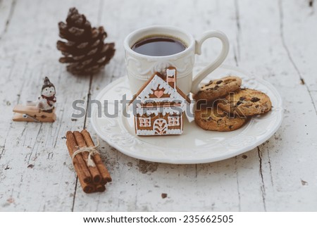 Shabby chic style coffee cup and plate with gingerbread house cookie, cinnamon sticks and other decorations for Christmas mood