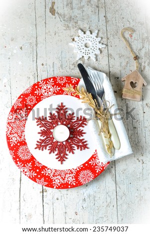 Christmas serving with red snowflake ornament plate, sparkling snowflake decor and tea-candle, with white napkin and cutlery wrapped in it an other christmas decorations