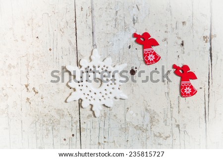 Christmas decor elements red wooden angels and white ceramic snowflake hanging on a white shabby wooden background