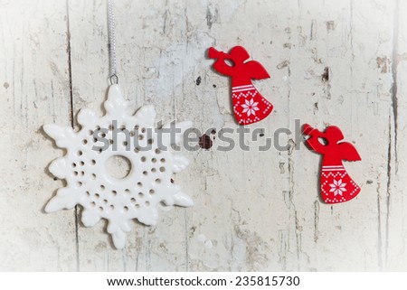 Christmas decor elements red wooden angels and white ceramic snowflake hanging on a white shabby wooden background