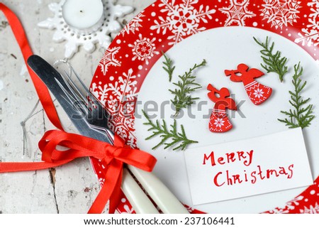 Christmas decorations with red plate snowflake ornament, cutlery tied with red ribbon and pine branch with christmas toys