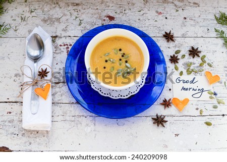 Pumpkin cream soup in a bowl  on a vintage plate with seeds and spices and good morning note, card