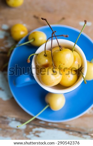 Blue tea cup full with yellow juicy cherries