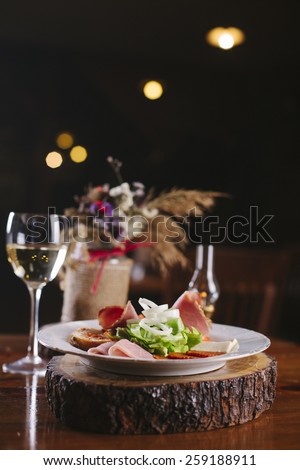 Appetizers - meat and cheese with lettuce and onion  - on wooden board with glass of white wine