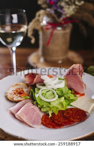 Appetizers - meat and cheese with lettuce and onion  - on wooden board with glass of white wine