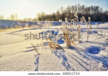 Winter landscape with sun and frozen river in sunset