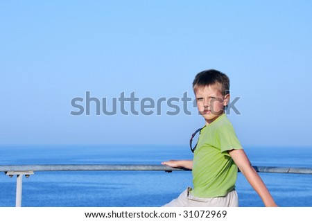 Happy young boy looking horizon and dreaming on quay of blue sea