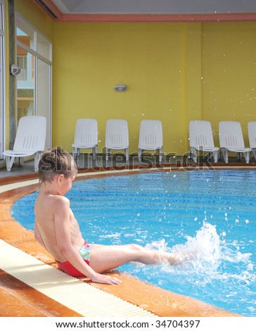Young boy swimming in the indoor pool sitting.