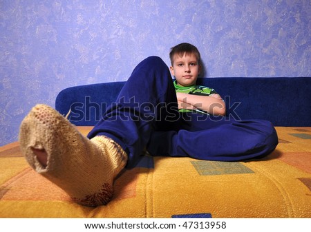 Boy wearing dirty socks with holes in them sits on sofa