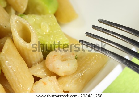 dish of Italian penne pasta with zucchini and shrimp and fork.Closeup of delicious food
